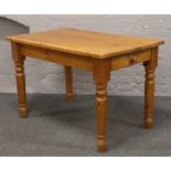A pine dining table raised on turned supports with single drawer to one end.