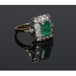 An 18 carat gold emerald and diamond ring. Set with a large baguette cut emerald under a border of