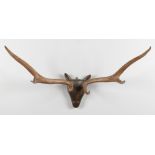 Two pairs of mounted stag antlers on carved wooden heads. Widest 105cm.