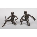 A pair of bronze figures Maasai warriors, each in crouched pose. One with a pair of swords and the