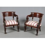 A pair of Victorian carved mahogany library armchairs. With swept backrests, scrolling arms