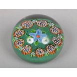 A Paul Ysart glass paperweight decorated with a flower under a cane garland over a green ground c.