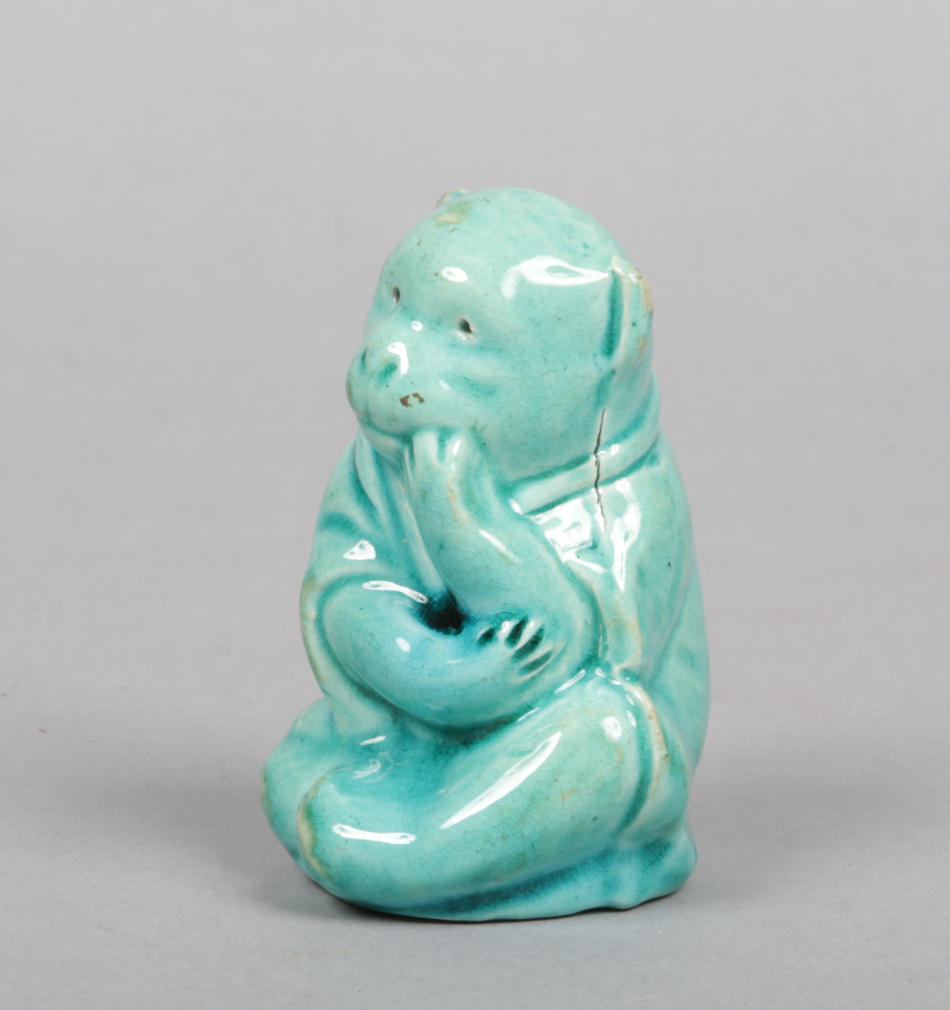 A Burmantofts Faience model of a seated monkey wearing an Oriental cape and decorated in turquoise