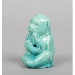 A Burmantofts Faience model of a seated monkey wearing an Oriental cape and decorated in turquoise