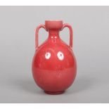 A Burmantofts Faience twin handled vase of amphora shape, glazed red and with incised repeat motifs.