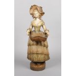 A large Goldscheider terracotta figure of a lady carrying a basket wearing a bonnet and a long