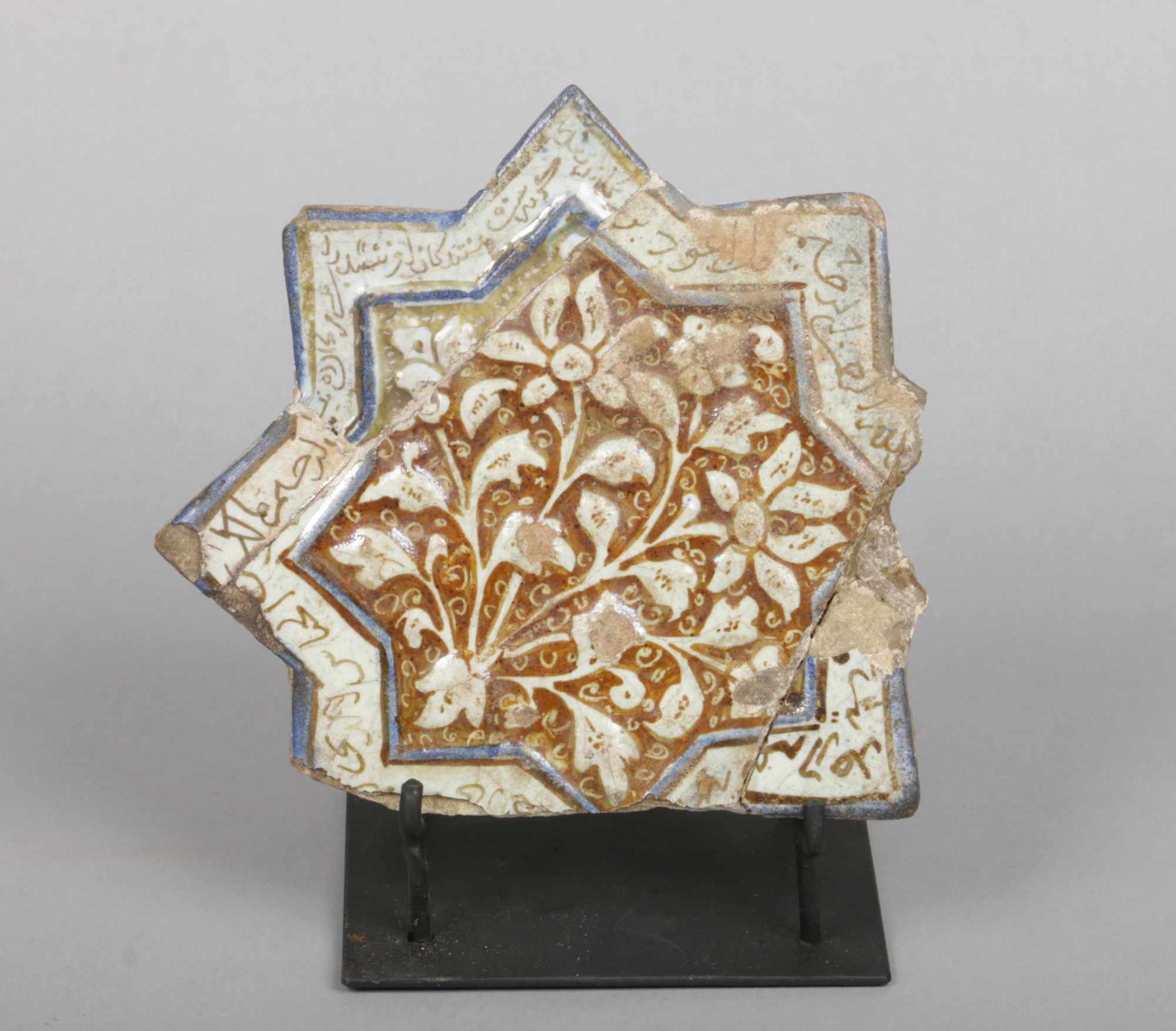 An antique Kashan star shaped tile on stand. Moulded with flowers and glazed in tones of turquoise