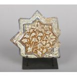 An antique Kashan star shaped tile on stand. Moulded with flowers and glazed in tones of turquoise