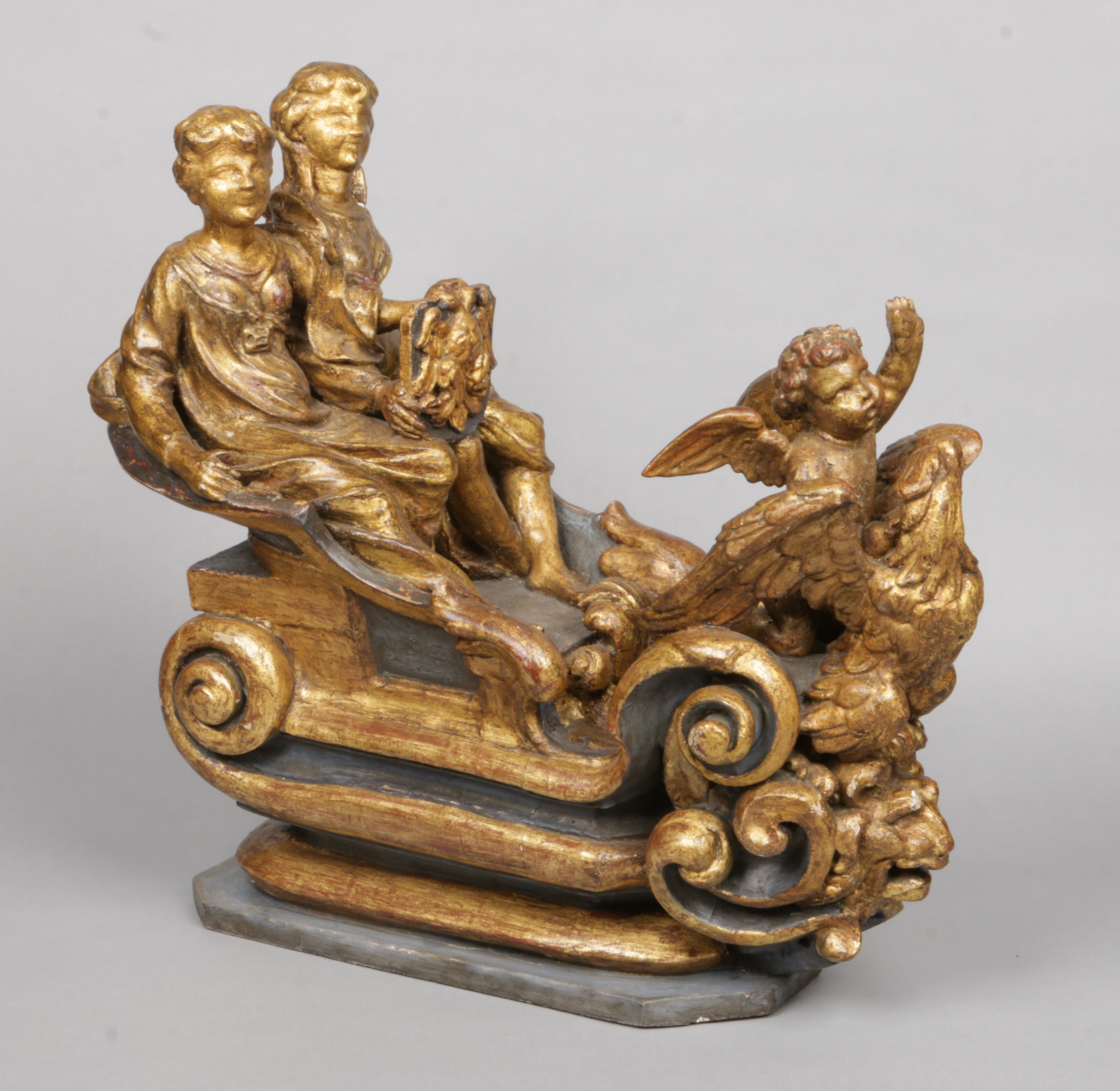 An antique Continental carved giltwood sculpture. Formed as two figures and a winged putti riding in
