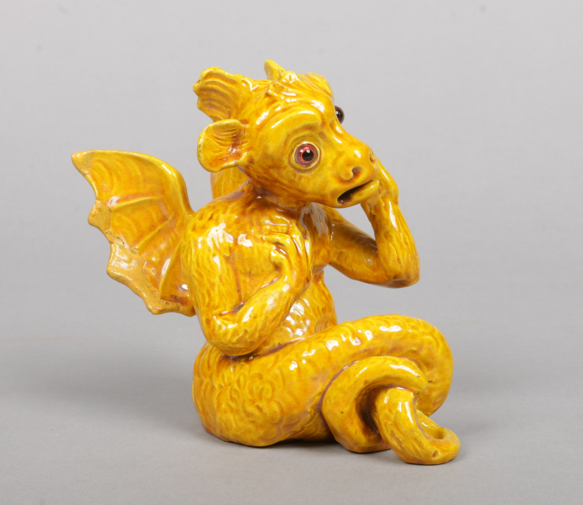 A Burmantofts Faience grotesque model of a winged gargoyle. Decorated in yellow glaze and with glass