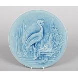 A Burmantofts Faience circular plaque. Modelled in low relief with a heron and frogs in a lake scene