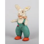 A Steiff Original mo hair rabbit. Wearing a bow tie, with green felt dungarees and orange shoes,