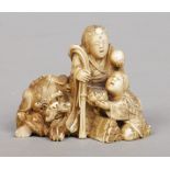 A Japanese Meiji period carved ivory netsuke. Modelled as a pair of figures and a recumbent lion