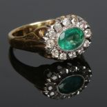 An 18 carat gold emerald and diamond halo cluster ring. The central emerald, set sideways measures