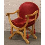 A carved oak scroll arm x framed chair with oval seat back, upholstered with claret coloured