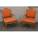 A pair of carved French armchairs with orange upholstery raised on cabriole legs.