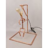 A copper pipe art work lamp formed as the hangman with large filament bulb.