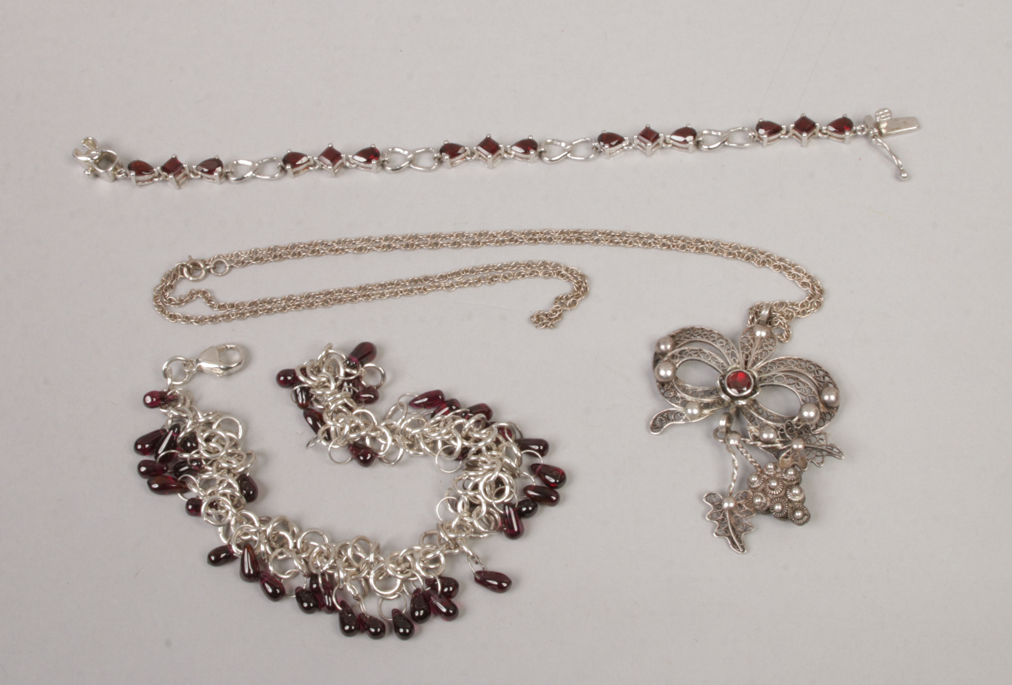 A garnet and silver filigree pendant on chain and two similar bracelets.