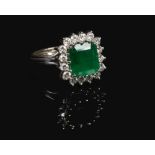 An 18 carat white gold emerald and diamond cluster ring. Set with a large square step cut emerald