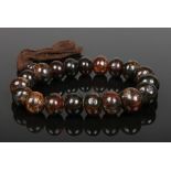 A string of brown amber ovoid prayer beads with natural inclusions and rope tassel. Largest bead