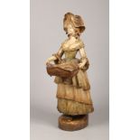 A large Goldscheider terracotta figure of a lady carrying a basket wearing a bonnet and a long