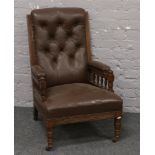 An Edwardian oak framed upholstered fire side armchair with deep buttoned back rest, raised on