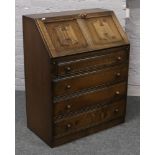 A carved oak linen fold bureau with fitted interior over four graduated drawers.