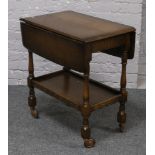 A carved oak drop leaf tea trolley with cutlery drawer raised on turned supports.