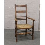 An ash ladderback arm chair with rush seat raised on turned supports.