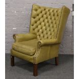 A olive deep buttoned leather porters wing arm chair raised on square cut legs.
