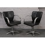 A pair of chrome and black vinyl swivel pneumatic salon chairs.