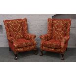 A pair of fireside wing arm chairs raised on carved ball and claw legs upholstered in period style