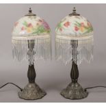 A pair of bronze effect table lamps with reverse hand painted glass shades, decorated with