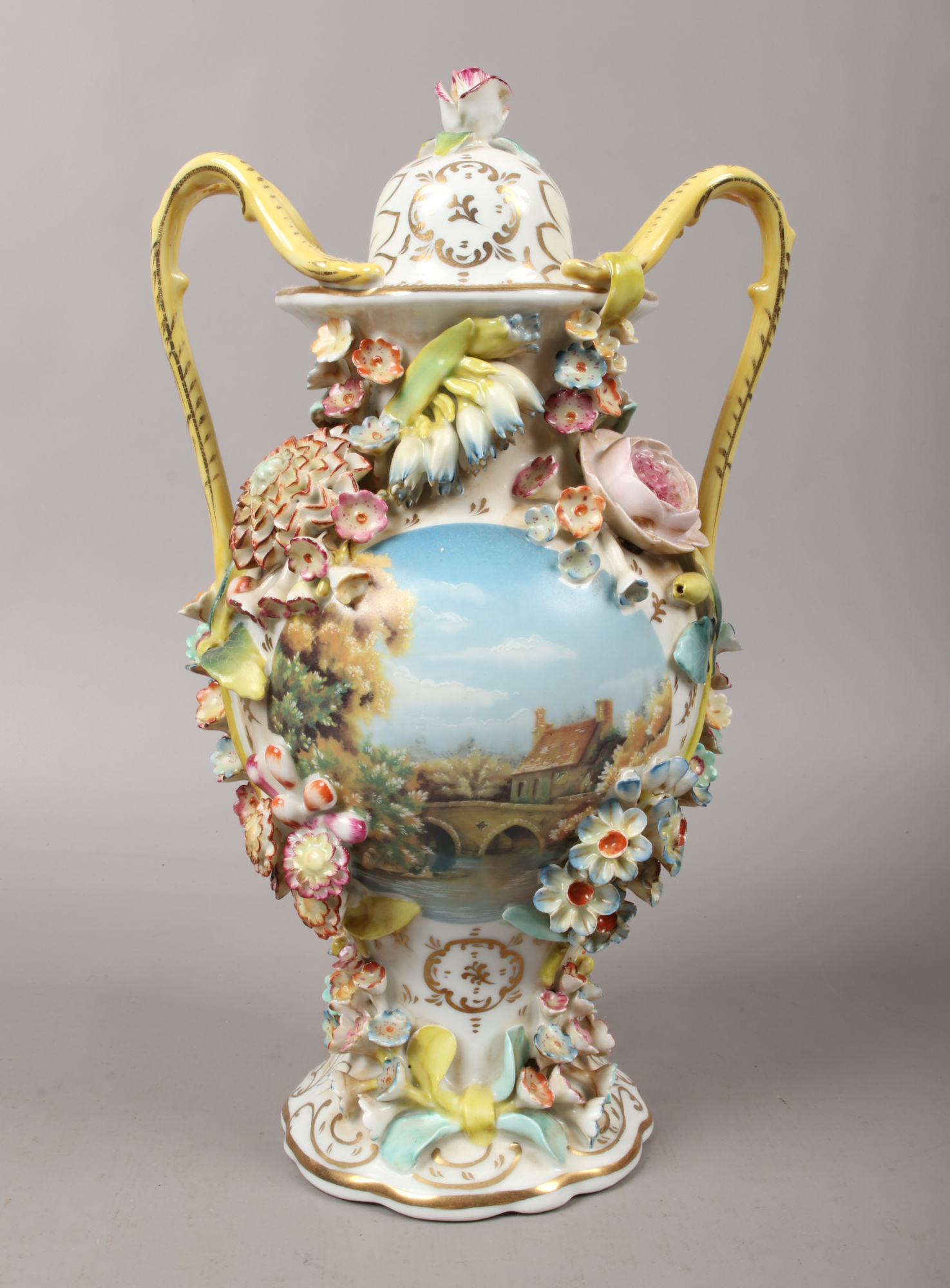 A Coalbrookdale china style urn decorated with a cottage view and applied flowers marked J.P to