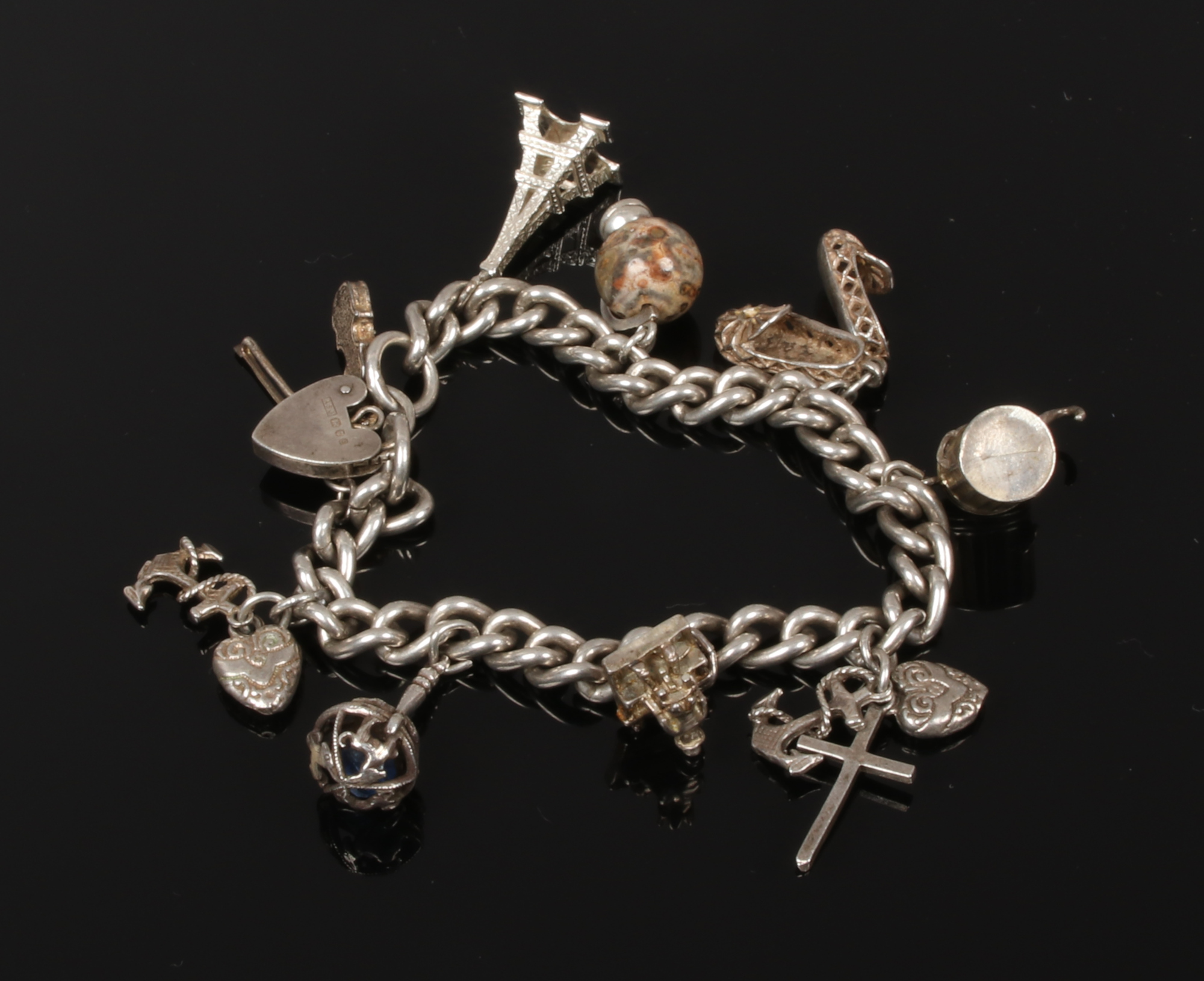 A silver charm bracelet on curb chain and with heart shaped clasp, 54 grams.