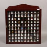 A display case of 100 collectors thimbles including bone china, split cane glass, cloisonne and