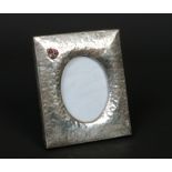 An Arts & Crafts planished white metal photograph frame on strut stand. Decorated with a trefoil