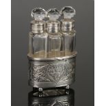 An early 20th century French trio of cut glass scent bottles in chased silver stand on ball feet.