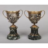 A pair of Continental 19th century silvered and gilt bronze twin handled urns raised on antico verde