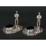 A pair of silver plated novelty figural salt sellers. Each surmounted with a footballer and a