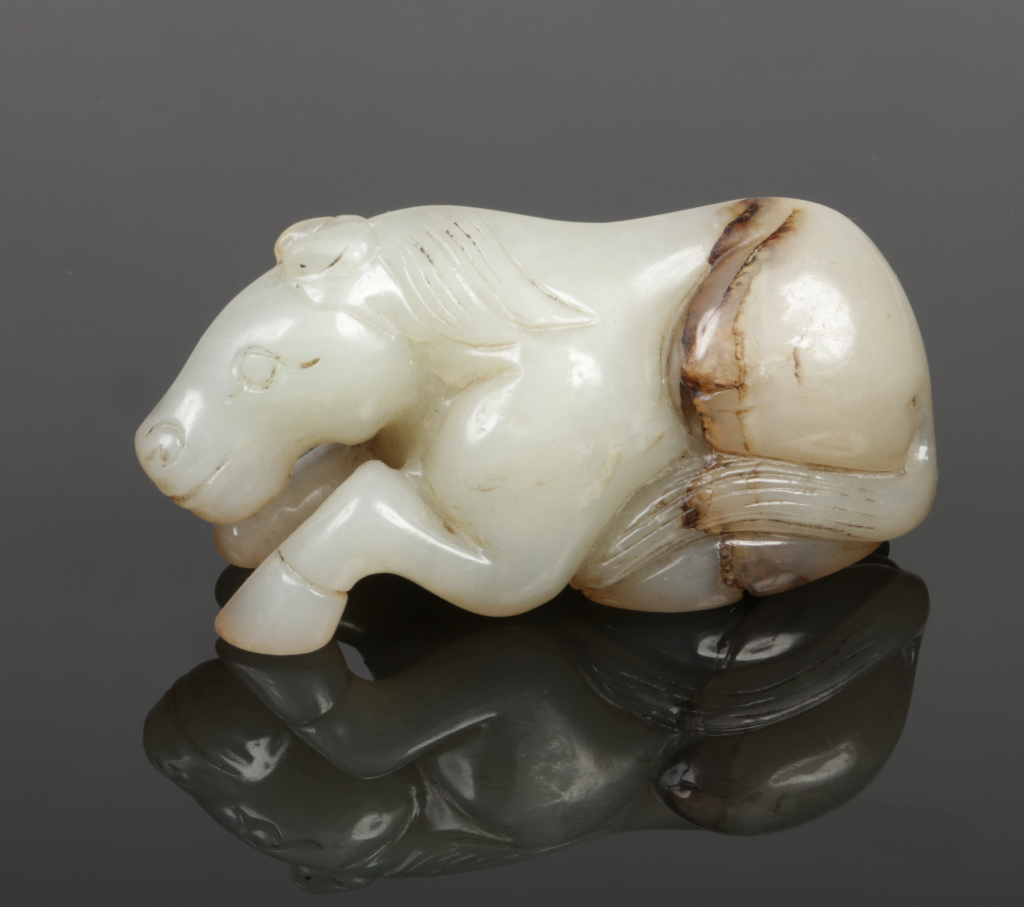 A Chinese carved pale celadon jade recumbent horse with dark brown suffusions, 7.75cm.Condition