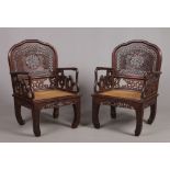 A pair of late 19th century Chinese hardwood elbow chairs with canework seats. Each with carved, and