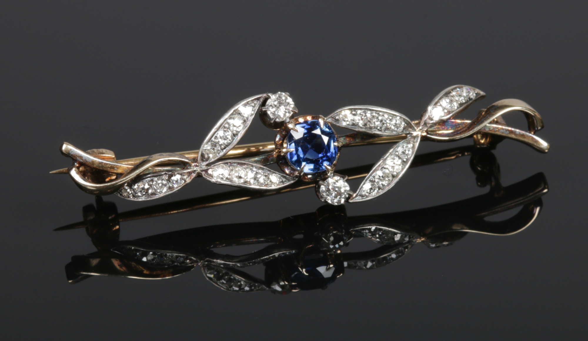 An Edwardian yellow metal bar brooch, with a central sapphire and leaf formed diamond studded