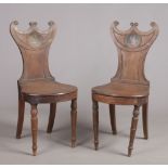 A pair of Regency mahogany hall chairs. With carved C-scroll cresting rails and each painted with