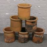Six square cylindrical terracotta chimney pots with rolled tops.