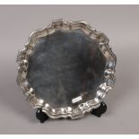 A silver plated salver with scalloped rim and raised on three scrolling feet.