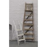 A pair of old wooden step ladders along with a aluminium set.