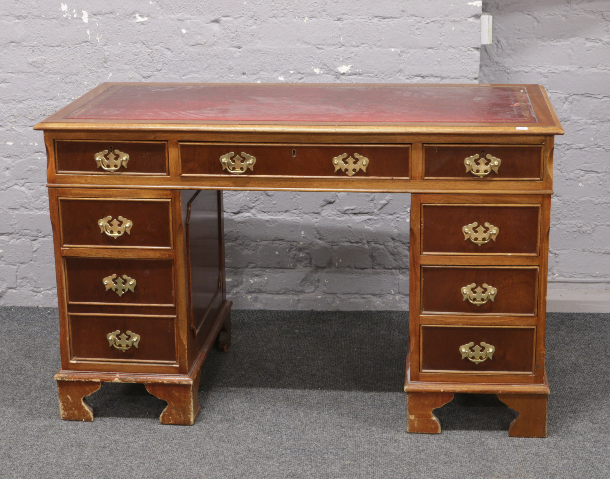 A mahogany pedestal desk with inset red leather top and brass metal mounts.