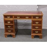 A mahogany pedestal desk with inset red leather top and brass metal mounts.