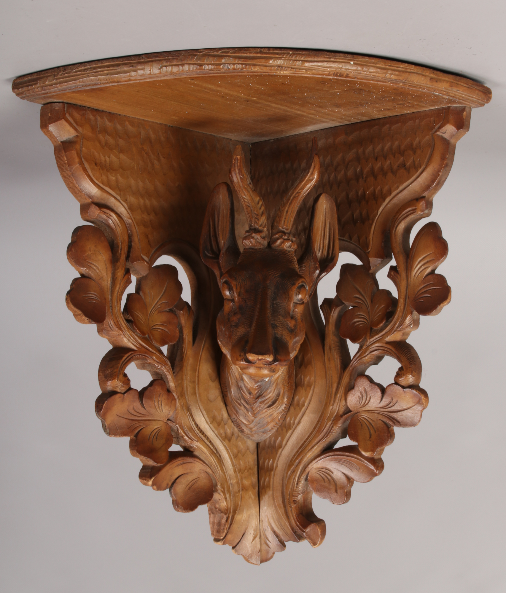 An early 20th century Black Forest corner bracket shelf, carved with the head of a Deer and acanthus